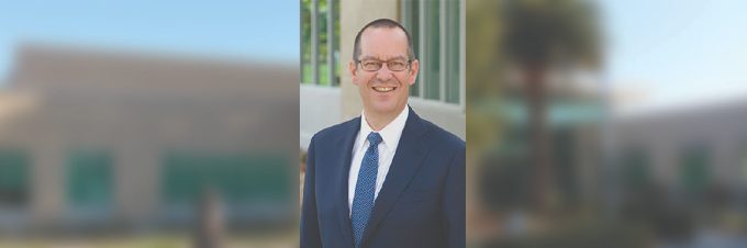 Chancellor Weispfenning, blue jacket and blue tie, in front of the Coast District building