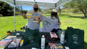 Two staff members in park setting wearing GWC t-shirts and holding GWC items.