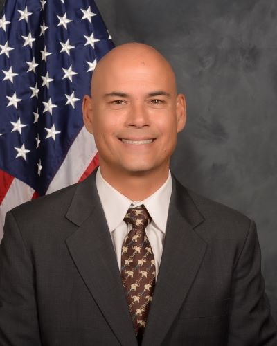 Portrait of Roy Sahachaisere in front of a flag.